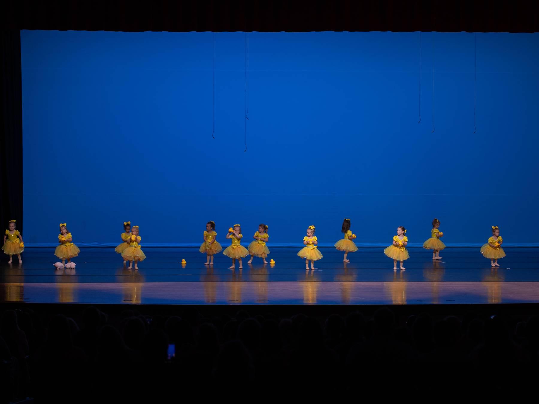 A long line of the youngest dancers in yellow tutus on a blue-lit stage