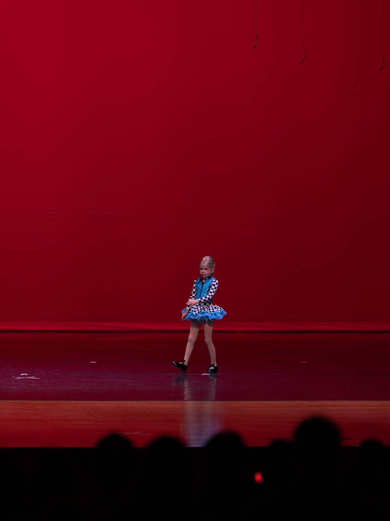 A dancer in a blue tutu performing alone in front of a red backdrop