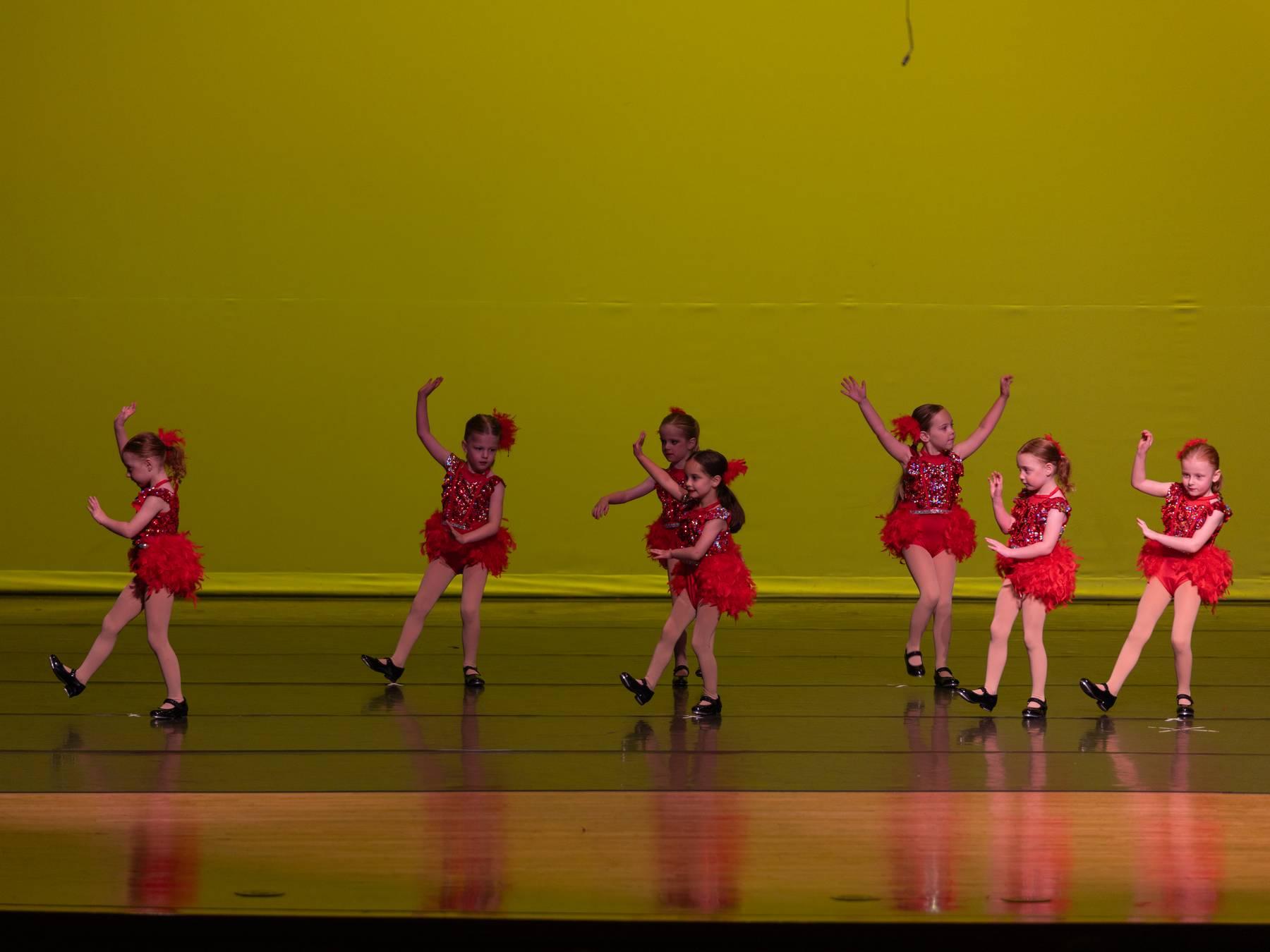 Young dancers in red sequined costumes on a yellow-lit stage