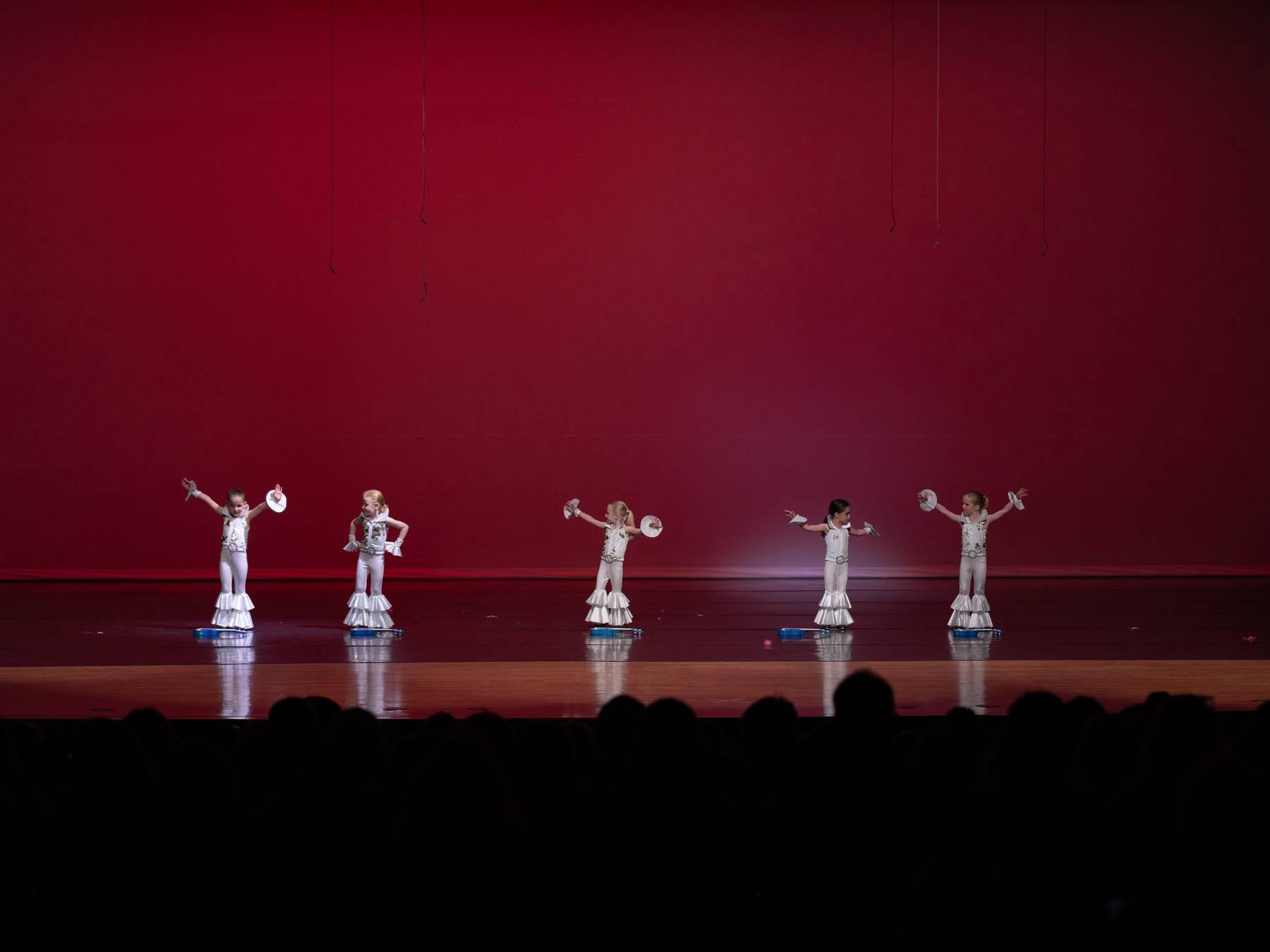 Dancers in white costumes spread across a red-lit stage
