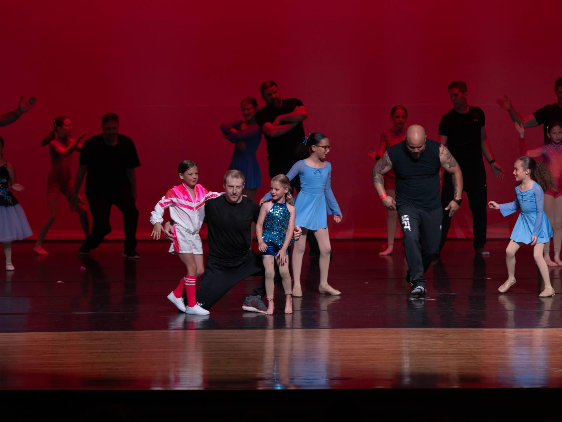Parents and dancers performing together on a red-lit stage